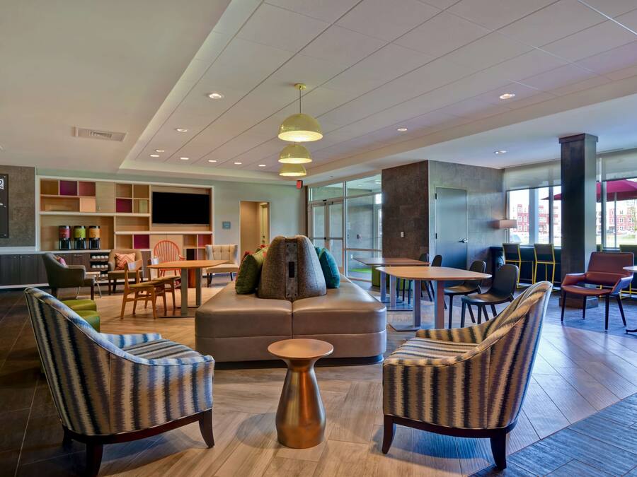 A modern lounge area with seating, a coffee station, and a large window providing a view of the city.