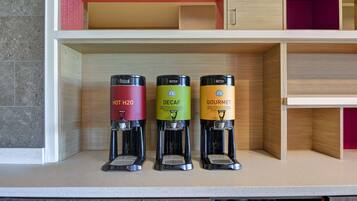 Três máquinas de café em uma bancada, cada uma identificada com diferentes tipos: Água Quente, Descafeinado e Gourmet.