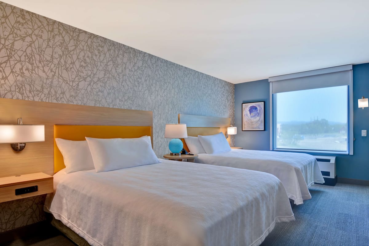 Ein Hotelzimmer mit zwei Betten, einem großen Fenster und Blick auf die Stadt sowie einer Wand mit Muster.