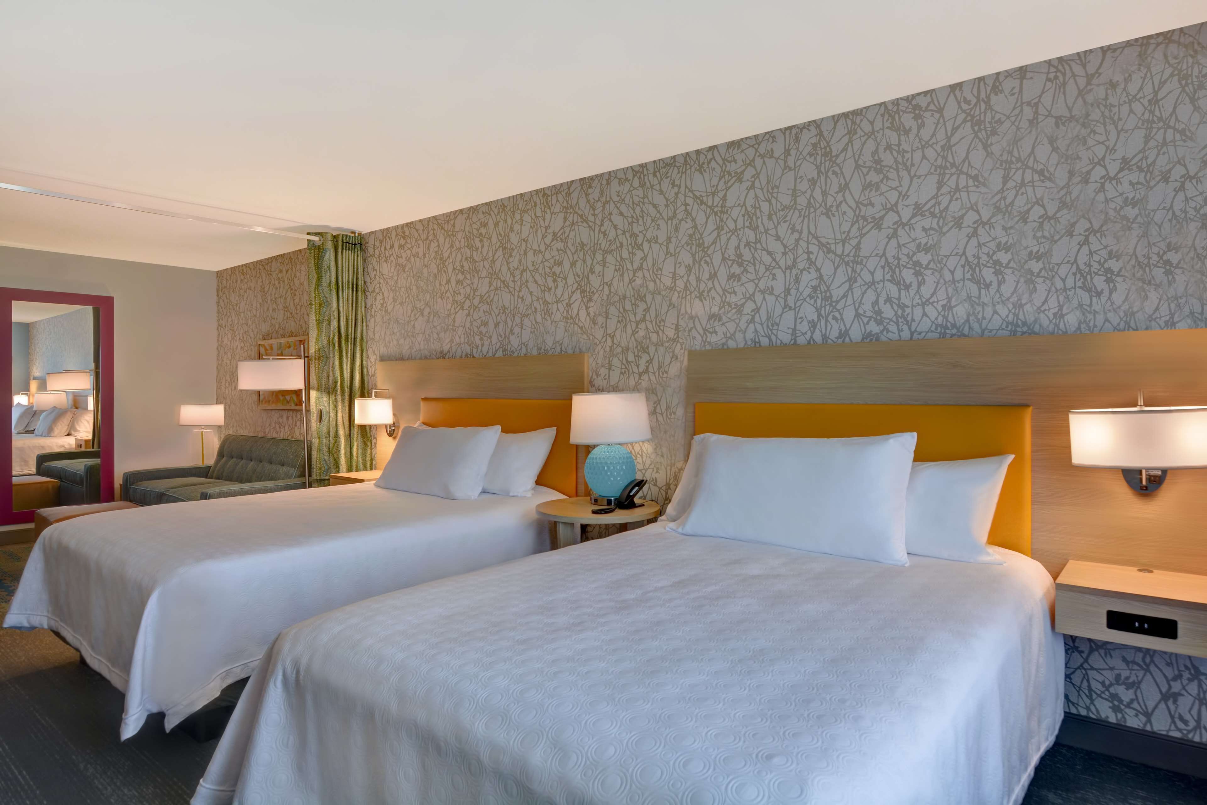 Una habitación de hotel con dos camas, un sofá, un espejo y un papel tapiz estampado.