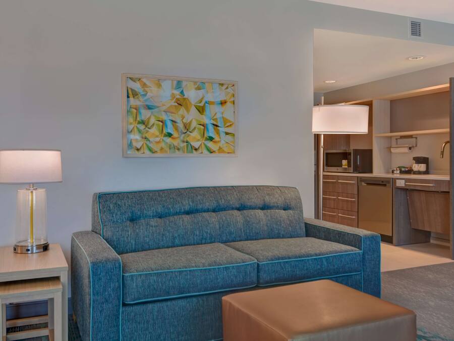Ein modernes Hotelzimmer mit einem blauen Sofa, einem kleinen Tisch, einer Lampe und einer Küche im Hintergrund.