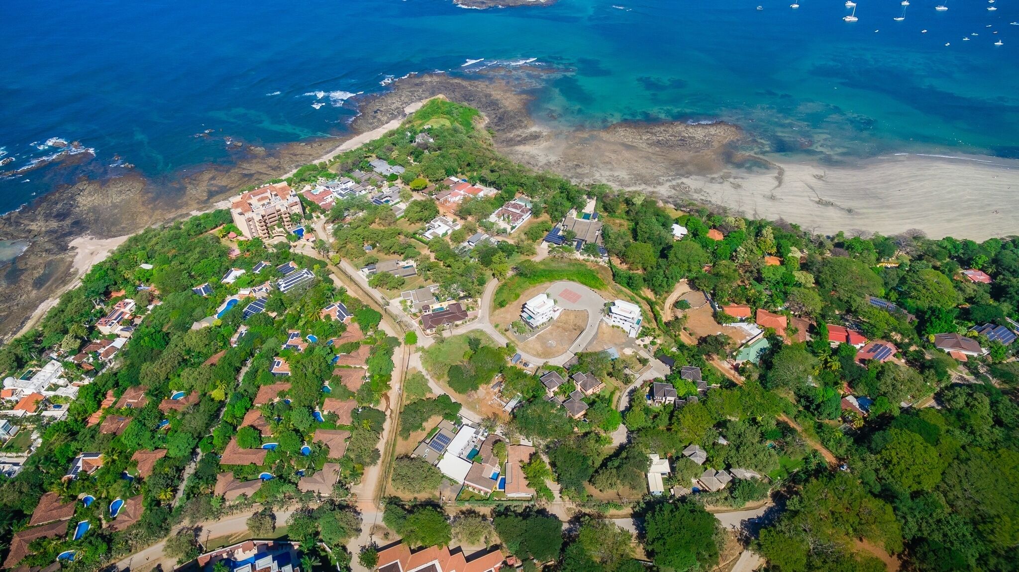Luchtbeeld van een kustgebied met woonhuizen, zonnepanelen en een strand.