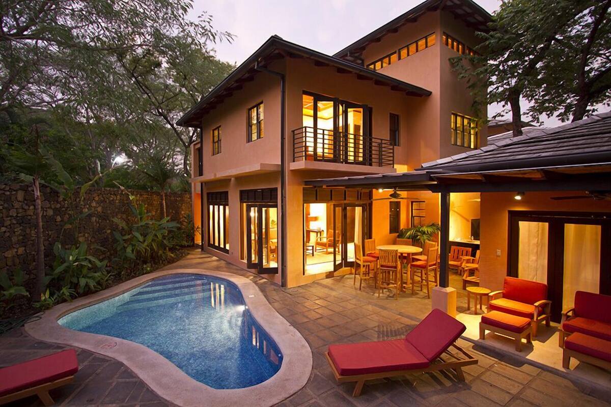 A two-story house with a swimming pool, outdoor seating, and a patio area.