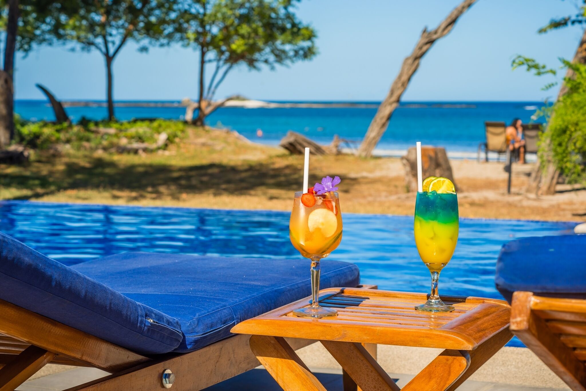 Zwei Liegestühle mit blauen Kissen und ein Tisch am Pool mit zwei Getränken.