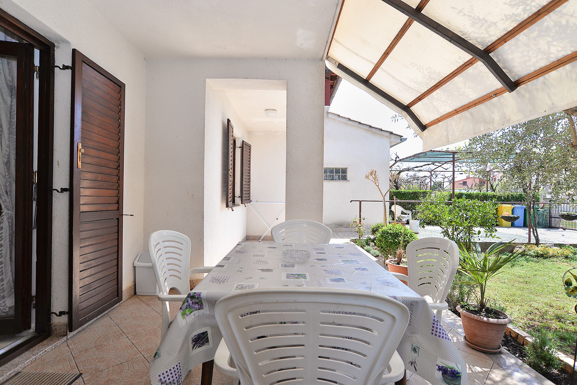 Une terrasse couverte avec une table et des chaises, une plante en pot et une vue sur les environs.