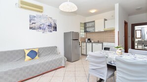 A compact living space with a kitchenette, a sofa with cushions, a dining table with chairs, and a ceiling light fixture. - Apartment 108/217 (Istria - Valbandon), 700m from the beach (Valbandon)
