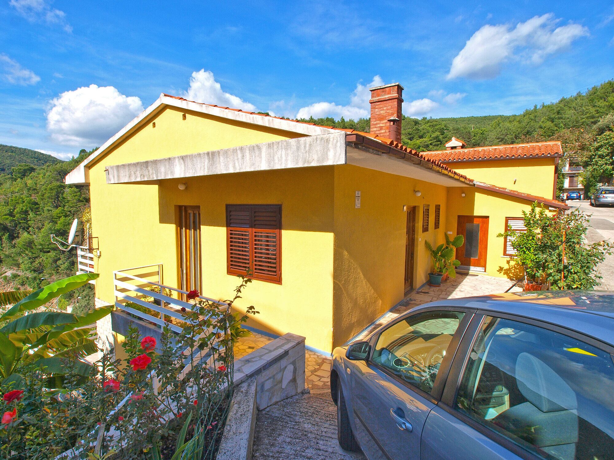 A yellow building with a red-tiled roof, a small porch, and a car parked in front.