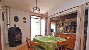A dining area with a green tablecloth, wooden chairs, a stone fireplace, and a kitchen visible through an open doorway. - Apartment 155/330 (Istria - Rabac), 500m from the beach (Rabac)