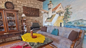 A living room with a stone wall, a fireplace, a sofa, a coffee table, and a large painting of a coastal scene. - Apartment 155/330 (Istria - Rabac), 500m from the beach (Rabac)