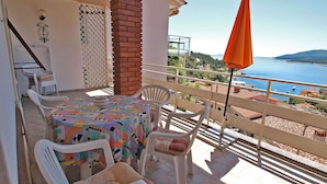 A balcony with a table and chairs, a brick pillar, a white chair with a cushion, and an orange umbrella. - Apartment 155/330 (Istria - Rabac), 500m from the beach (Rabac)