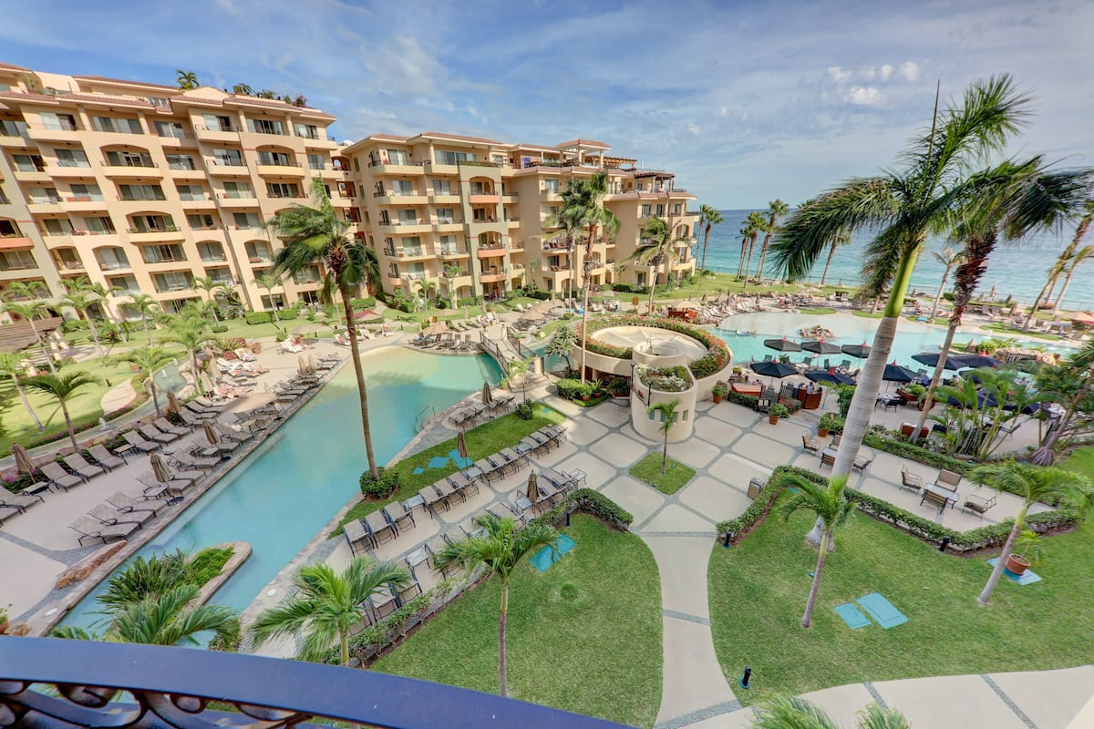 Un hotel con varios balcones, piscina central y un jardín circundante.