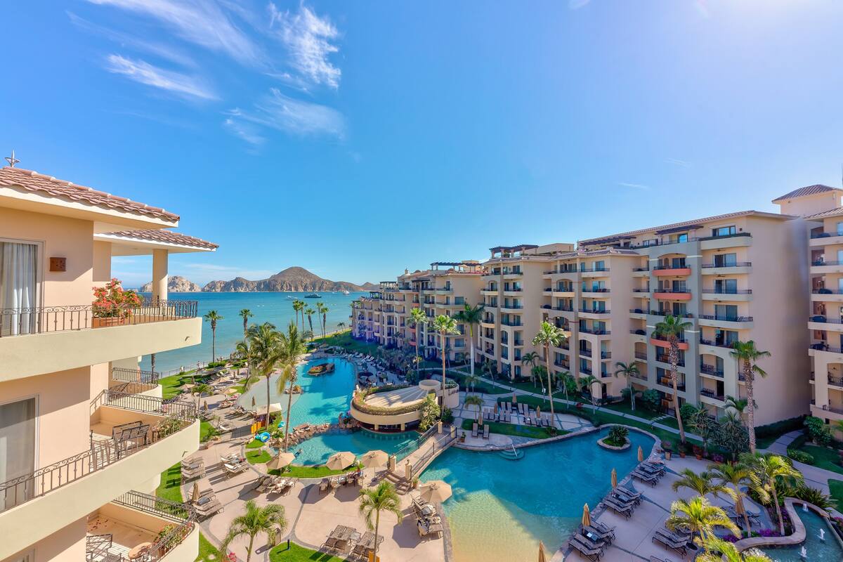 Un resort con varios balcones, una piscina central y vista al océano.