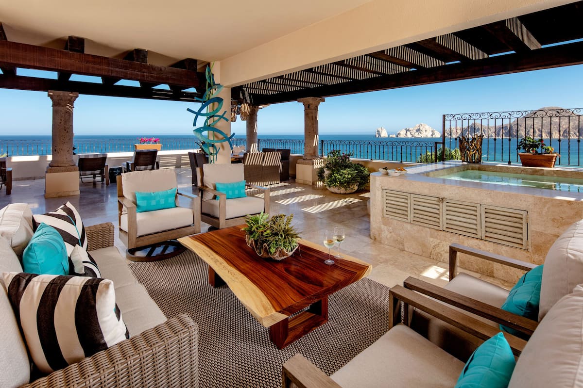Un amplio espacio al aire libre con una mesa de centro de madera, sillas de mimbre y vistas al mar.