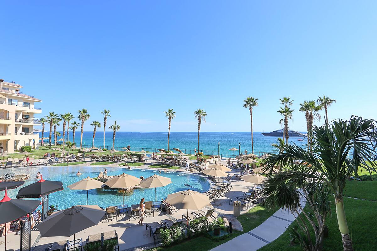 Un resort con una piscina grande, palmeras y vistas al océano.