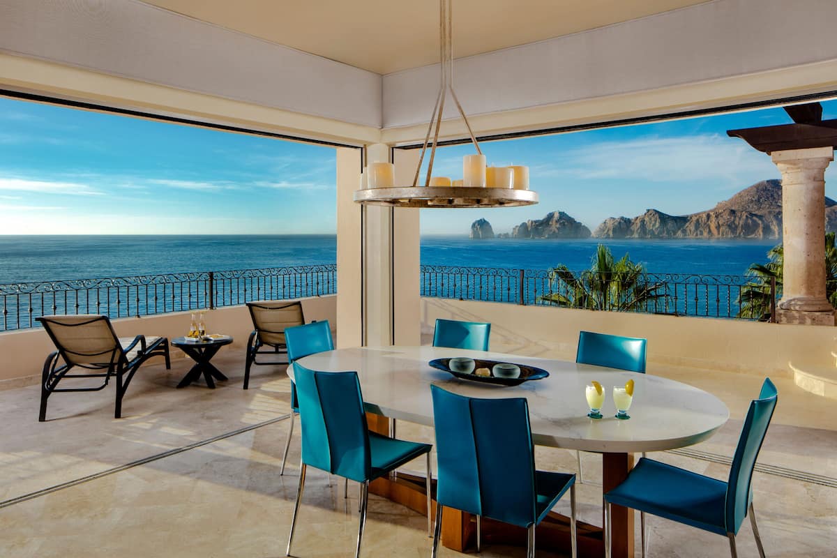 Comedor con vista al mar, que incluye una mesa redonda, sillas azules y una lámpara colgante.