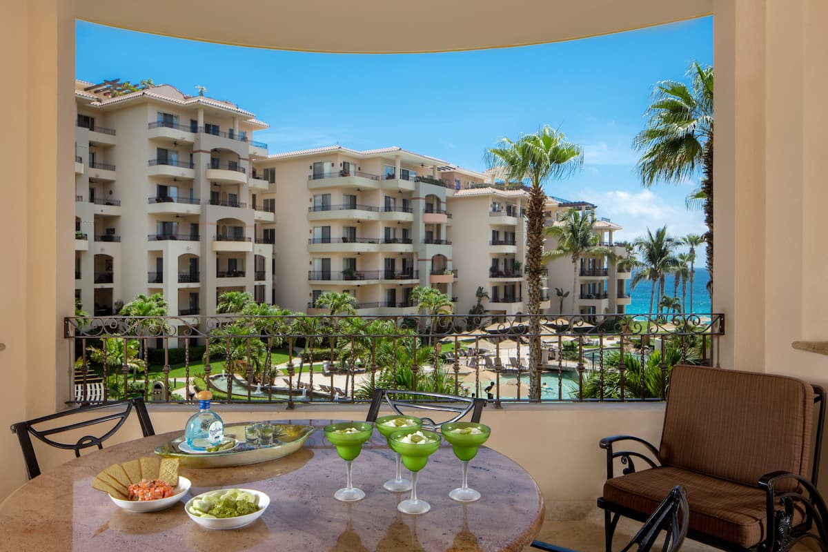 Un balcón con una mesa lista para una comida, con vista a un resort con varios edificios y una piscina.