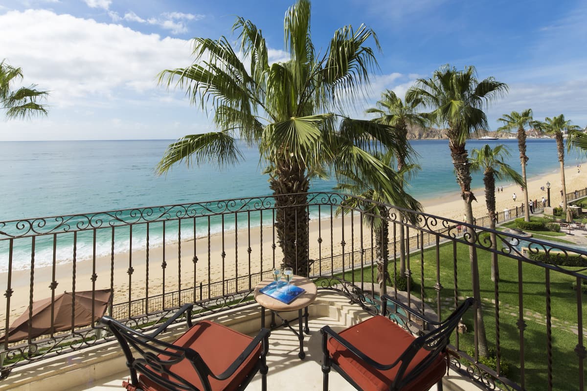 Un balcón con vista a la playa, palmeras y una mesa con sillas.