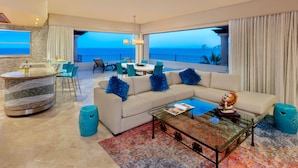 A modern living room with a large sofa, a coffee table, and a dining area. There is a view of the ocean through large windows. - Cabo La Estancia (Cabo San Lucas)