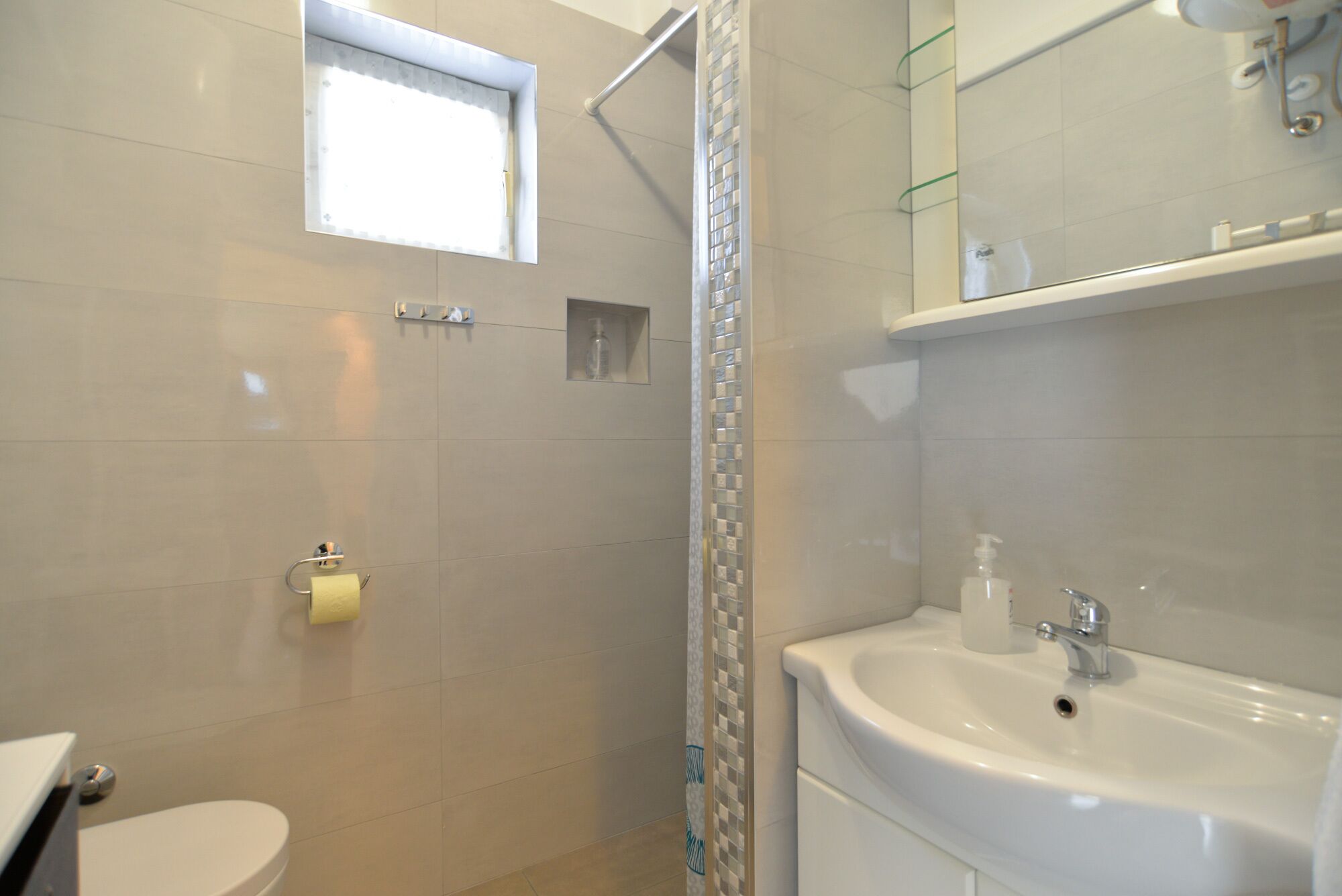 A bathroom with a toilet, a sink, a shower with a glass door, and a small window.