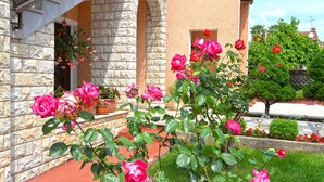 Un bâtiment en pierre avec un chemin bordé de briques rouges et des rosiers roses au premier plan.