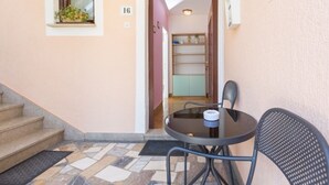 A small outdoor seating area with a table and chairs, a window with plants, and a staircase leading to an interior room.