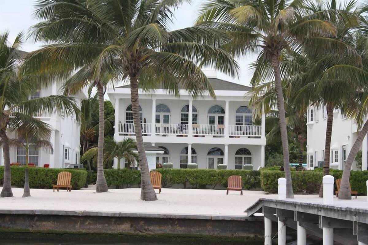 Un bâtiment de style colonial blanc, doté de nombreux balcons, entouré de palmiers et bordé d’une plage de sable.