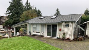 A house with a covered porch, a sliding glass door, and a small garden area with potted plants. - The Lake Tapps Bungalow (Lake Tapps)