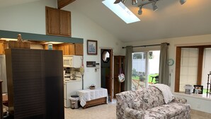 A cozy living room with a floral sofa, a quilted bed, and a kitchen area with wooden cabinets and a microwave. - The Lake Tapps Bungalow (Lake Tapps)