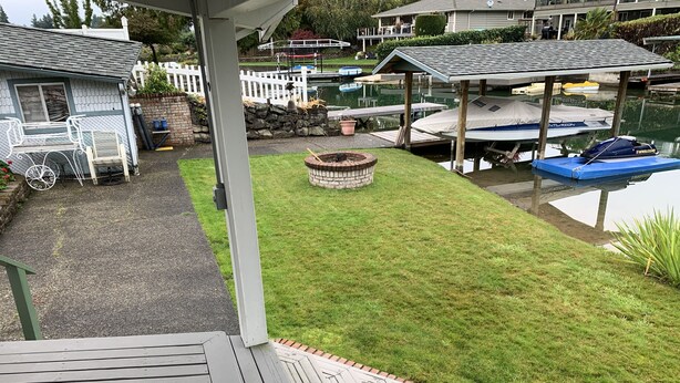 A deck with a fire pit, a covered seating area, and a view of a dock with boats. - The Lake Tapps Bungalow (Lake Tapps)