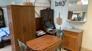 A room with a wooden dining table, chairs, a wooden cabinet, a computer desk, and a bed with a blue and white quilt. - The Lake Tapps Bungalow (Lake Tapps)