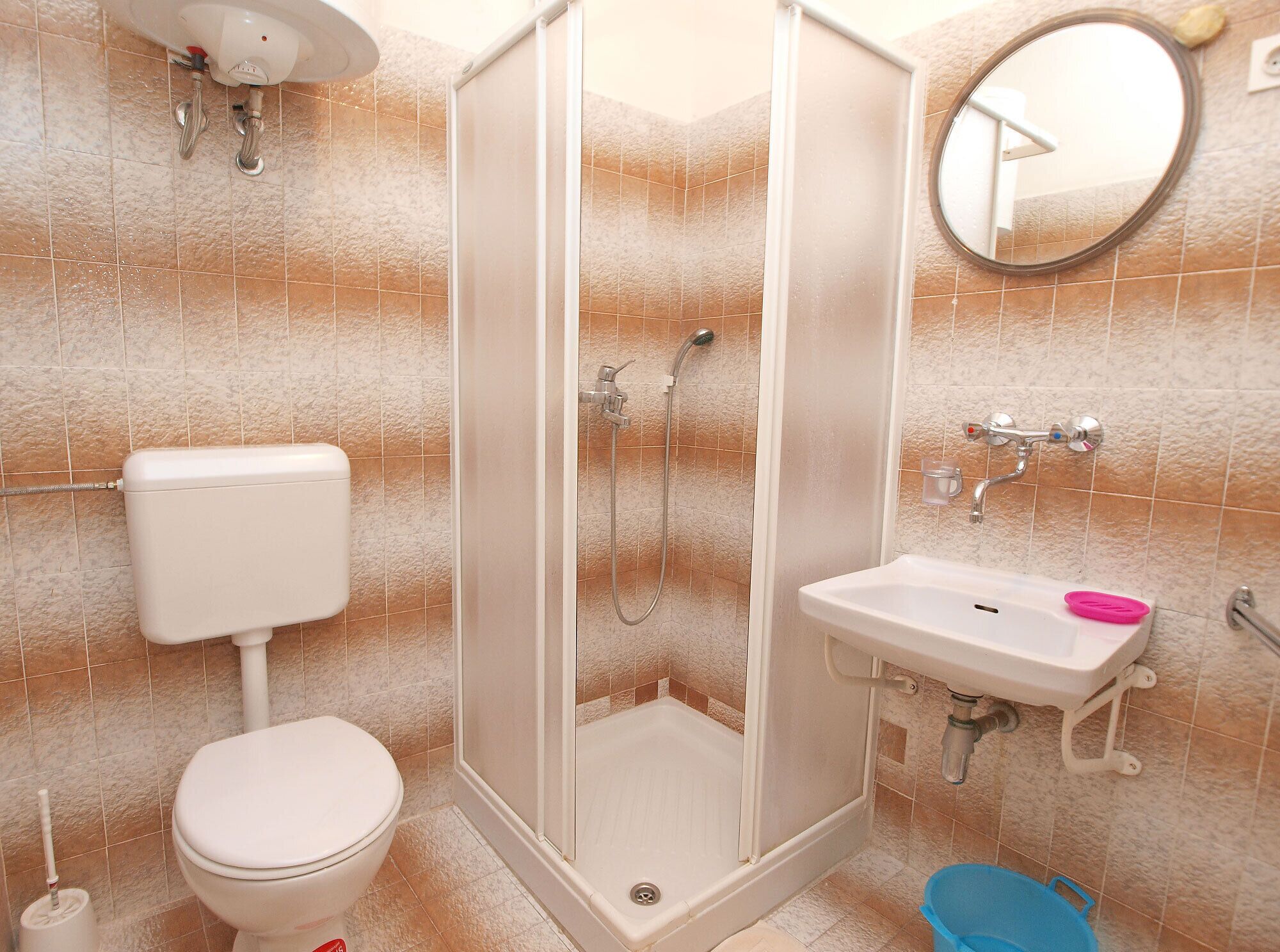 Baño con inodoro, ducha, lavamanos y espejo.