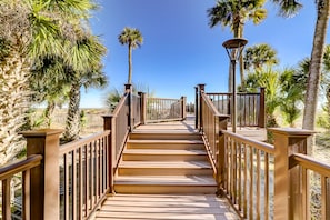 A wooden boardwalk leading to a beach with palm trees and a clear blue sky.