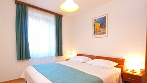 A neatly made bed with a blue and white bedspread, a wooden headboard, and a nightstand with a lamp. - Apartment 279/619 (Istria - Vrsar), 100m from the beach (Vrsar)