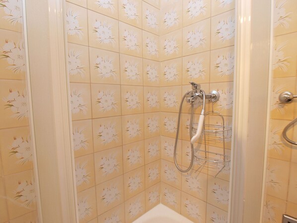 A shower with a floral tile pattern, a handheld showerhead, and a wall-mounted faucet.