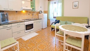 A compact kitchen with a stove, oven, and refrigerator, a dining area with a table and chairs, and a window with curtains. - Apartment 279/619 (Istria - Vrsar), 100m from the beach (Vrsar)