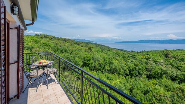 A balcony with a table and chairs, overlooking a lush green landscape and a body of water. - Apartment 294/648 (Istria - Labin), 800m from the beach (Labin)