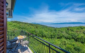 A balcony with a table set for breakfast, overlooking a lush green landscape and a body of water.