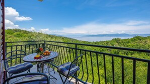 Un balcone con un tavolo apparecchiato per la colazione, con vista su un paesaggio lussureggiante e un corpo d'acqua.
