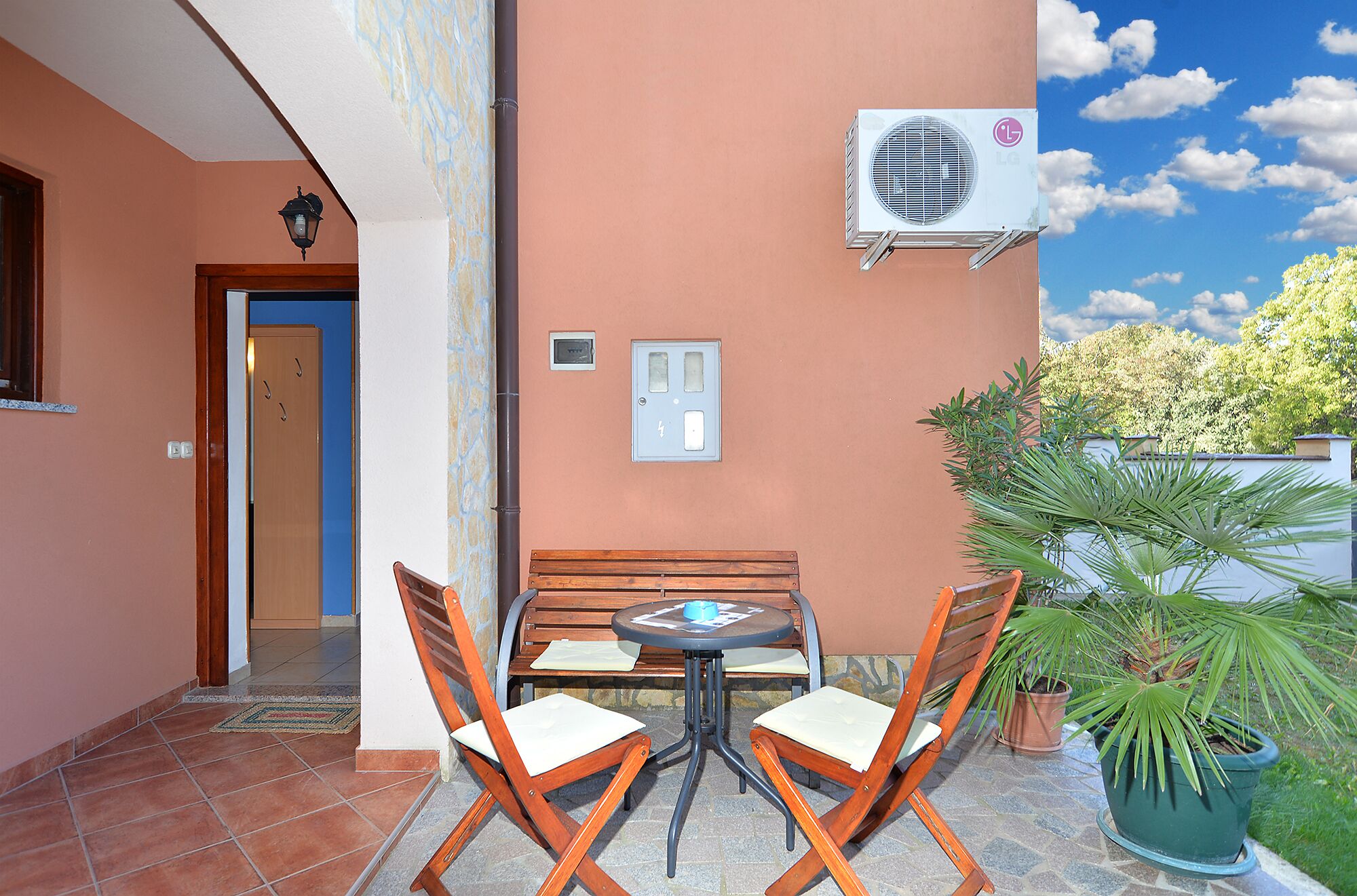 Une terrasse avec une table et des chaises, un appareil de climatisation, une porte et une boîte électrique fixée au mur.
