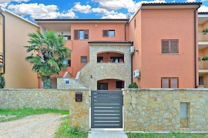 A two-story building with a stone facade, a gated entrance, and a small balcony with potted plants.