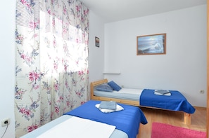 A bedroom with two single beds, a wooden headboard, a painting on the wall, and a floral curtain.