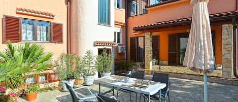 Un patio con una mesa y sillas, rodeado de plantas en macetas y una sombrilla.
