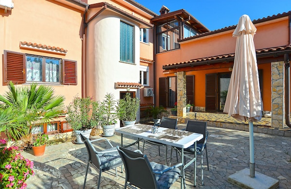 A patio with a table and chairs, surrounded by potted plants and an umbrella.