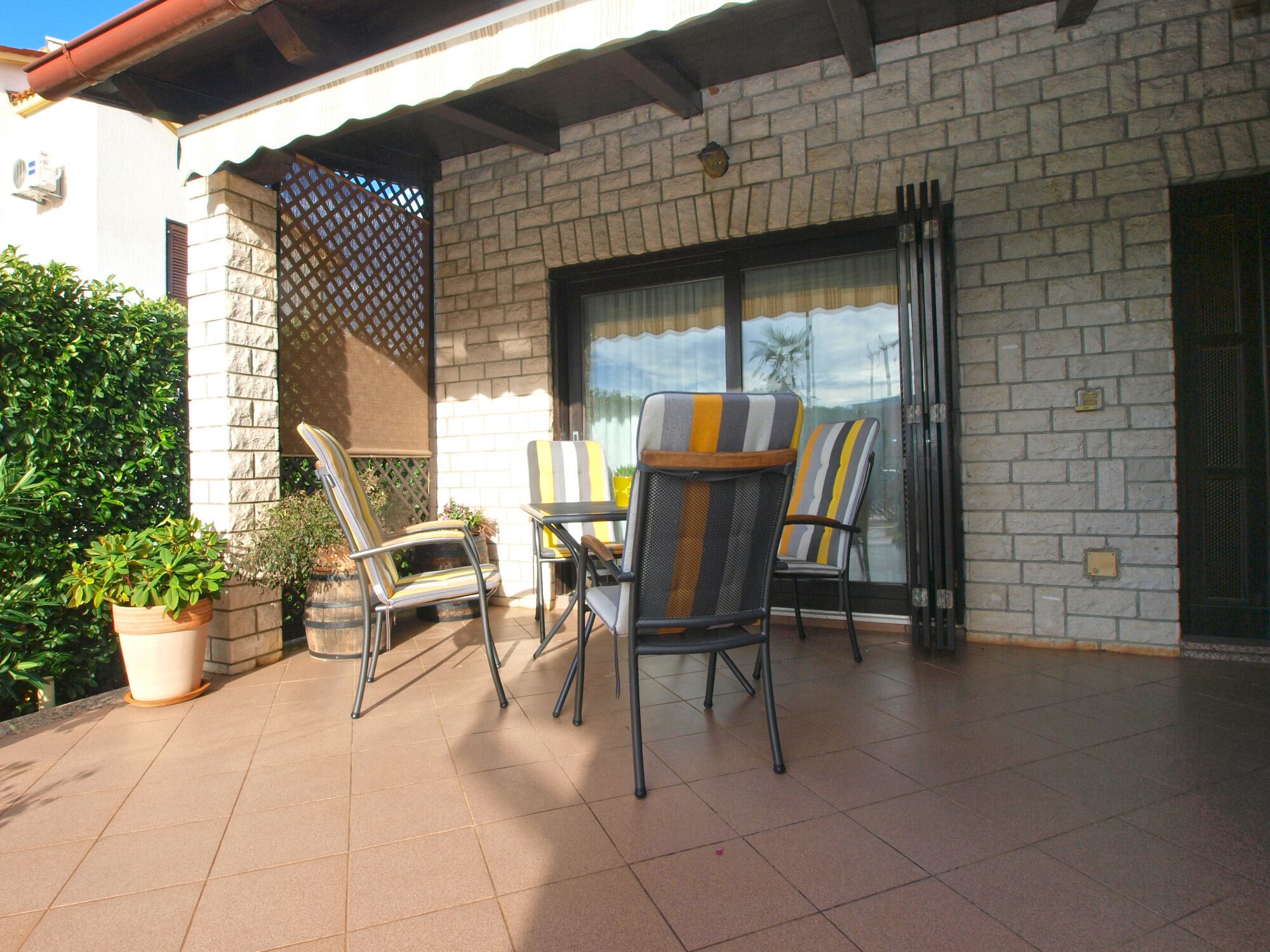 Un patio con suelo de baldosas, mobiliario exterior que incluye sillas y una mesa, y una planta en maceta.