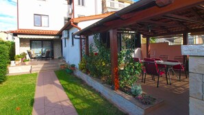 A patio area with outdoor furniture, a stone wall, and a pathway leading to a building with a tiled roof.