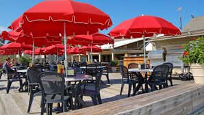 Outdoor tables and chairs with red umbrellas, a barbecue grill, and a wooden deck.