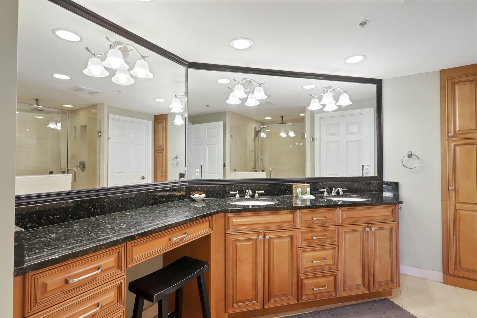 A bathroom with a large mirror, two sinks, wooden cabinets, and a black countertop.