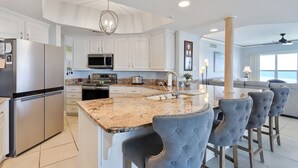 A modern kitchen with white cabinetry, stainless steel appliances, a granite countertop, and a bar area with tufted chairs.