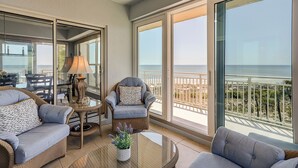 A balcony with wicker furniture, a glass table, and a view of the ocean.