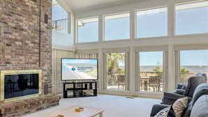 Amplia sala de estar con chimenea de ladrillo, televisor de pantalla plana y balcón con mobiliario exterior.